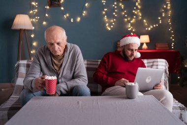 Yaşlı ebeveynler için zaman yok. Oğlu dizüstü bilgisayarda çalışıyor, yaşlı babasıyla koltukta oturuyor, babasını görmezden geliyor, çocuğu tarafından ihmal edildiğini düşünüyor. Boşluğu kopyala