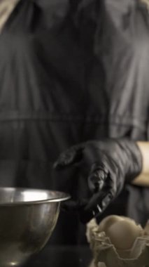 Fırında yemek pişirmek için siyah önlüklü kadın fırıncı yumurta kırıyor, yakın plan. Dikey video