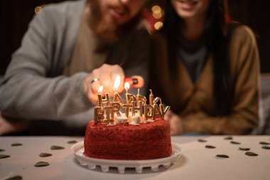 Man lighting happy birthday candles burning on a cake. Close-up. Selective focus clipart