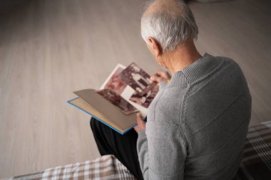 Albümdeki eski fotoğraflara bakan yaşlı bir adamın oturma odasındaki koltukta oturduğu en iyi manzara. Boşluğu kopyala