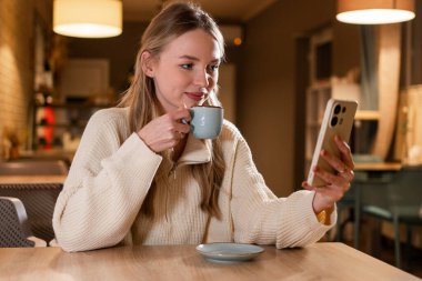 Genç bir kadın süveter giyer, cep telefonu içer kahve içer, dinlenir ve boş zaman geçirir. Boşluğu kopyala