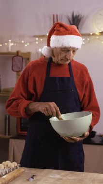 Yaşlı kıdemli adam Noel kurabiyeleri için hamur topluyor, emekli fırıncı kış tatillerinde sıcacık mutfakta yemek pişiriyor, Noel tatlısı yapıyor. Dikey video