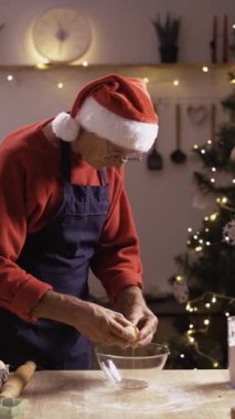 Yaşlı kıdemli adam Noel kurabiyeleri için hamur topluyor, emekli fırıncı kış tatillerinde sıcacık mutfakta yumurta pişiriyor, Noel tatlısı yapıyor. Dikey video