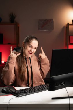 Female programmer wearing hoodie working overtime shouting with crazy expression doing rock symbol with hands at home. Copy space clipart