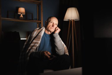Yaşlı adam gece oturma odasında sandalyede otururken uzaktan kumandayla televizyon kanallarını değiştiriyor. Boşluğu kopyala