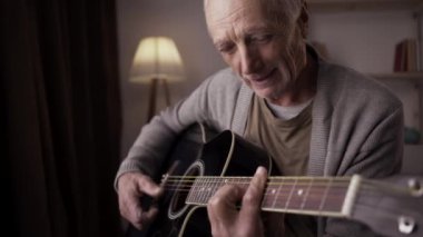 Yaşlı adam gitarda müzik çalışıyor. Evde akustik gitar çalan son sınıf erkek gitarist. Yakın plan.