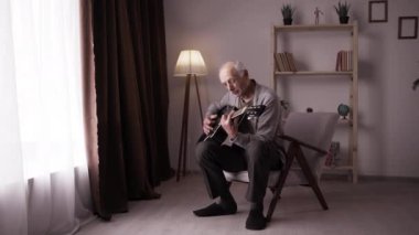 Yaşlı bir adam bir evin oturma odasında bir sandalyede oturup gitar çalarak şarkı söylüyor. Boşluğu kopyala