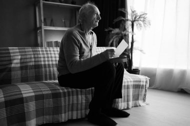 Yalnız, hayalperest yaşlı adam kanepeye oturmuş fotoğraf albümündeki fotoğrafa bakıyor. Yalnızlık ve anılar konsepti. Siyah beyaz fotoğraf