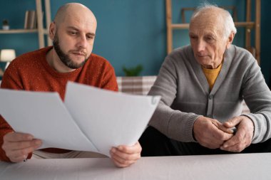 Yetişkin sakallı bir adam, babasından mali evrakları ve faturaları almasına yardım ediyor. Yakın plan.