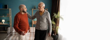 Yaşlı bir baba, oturma odasında ayakta dururken zorluklarla başa çıkmasına yardımcı olmak için yetişkin oğlunu rahatlatıyor ve geçindiriyor. Pankart. Boşluğu kopyala