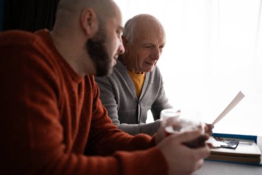 Yaşlı adam ve oğlu birlikte bir fotoğraf albümüne bakıyorlar. Erkek aile fotobook izliyor. Baba oğul birlikte vakit geçiriyor. Uzayı kopyala Yan görünüm