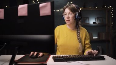 Gözlüklü yetişkin kadın oyuncu kişisel bilgisayarında online video oyununda bir tur oynuyor. Profesyonel oyuncu gülümseyen bir öpücükle şampiyonluğun tadını çıkarıyor.