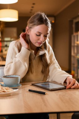 Kafe 'de dijital tablet kullanan sarışın bir kadın bilgisayarında yeni bir proje yaratıyor. Boşluğu kopyala