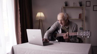 Akustik gitar çalıp evde online kurs izlemeye odaklanmış bir büyükbaba. Çevrimiçi eğitim kavramı