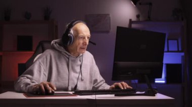 Yaşlı emekli adam bilgisayar oyunu kurgusu kullanarak online oyunlar oynuyor ve evde iyi vakit geçiriyor. Çevrimiçi kulaklık takan oyuncu.