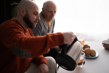 Aile babası ve oğlu evde çay içiyor. Yetişkin bir adam çaydanlıktan yaşlı babası için fincanlara çay dolduruyor. Boşluğu kopyala