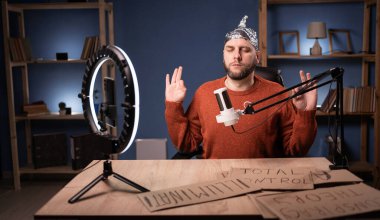 Crazy conspiracy theorist blogger streaming live at home using smartphone and ring light, meditation has zen sitting at the table. Copy space clipart