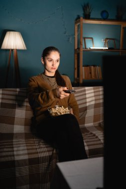 Kanepede oturan, patlamış mısır yiyen ve evde televizyon izleyen bir kadın. Kadın izleyici uzaktan kumandası film izlemekten zevk alıyor. Boşluğu kopyala