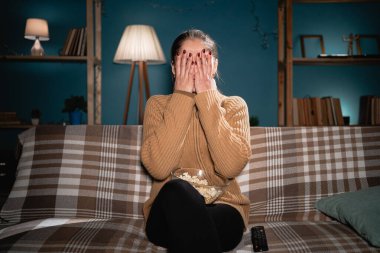 Televizyon dehşeti. Şok olmuş kadın heyecandan korkan elleriyle yüzleri kapatıyor. Geceleri evde film izleyen ürkek bir kadın. Boşluğu kopyala