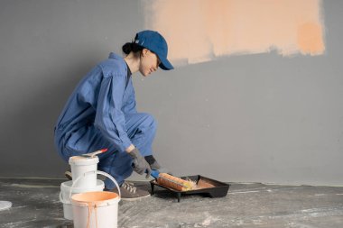 Bir sanatçı boya silindiriyle duvar boyar. İnşaat işçisi yüzeyi açık renkli boyar. Boşluğu kopyala