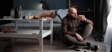 Yetişkin bir adam, evde oturmuş, bir şişe viski içiyor. Yorgunluk. Alkol bağımlılığı. Boşluğu kopyala