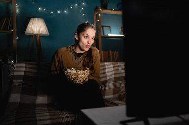 Şaşırmış bir kadın gece ilginç bir film izlerken evde patlamış mısır yiyor. Boşluğu kopyala