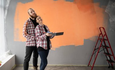 Mutlu çift duvarı boyuyor ve mesaj için uzaya bakıyor. Aile babası ve kadın yeni evde tadilat yapıyorlar. Boşluğu kopyala