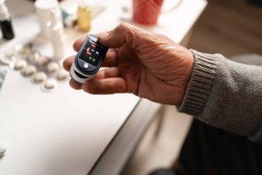 Yaşlı adam kan oksijeni seviyesini ölçmek için nabız oksimetresi kullanıyor. Akciğerlerinde sorun var. Yakın plan.