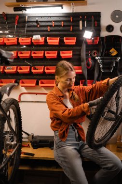 Bisiklet atölyesinde dikilirken bisiklet tekerleğini tamir eden beyaz kadın tamirci. Boşluğu kopyala