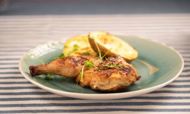 Kızarmış patates yarısıyla servis edilen sulu ızgara tavuk yeşil tabakta. Taze otlarla süslenmiş bu yemek, sağlıklı bir yemek için mükemmel tat ve dokuları birleştirir..