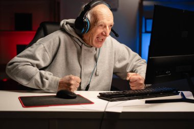 Öfkeli bilgisayar oyuncusu, kulaklık takan emekli bir adam online video oyununda yenildikten sonra bağırıyor. Boşluğu kopyala