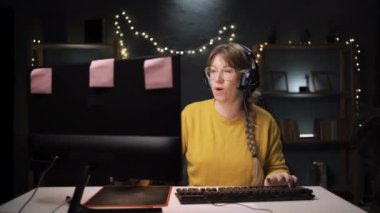 Kulaklıklı ve gözlüklü video oyuncusu bir kadın çevrimiçi canlı yayın sunuyor aboneleriyle sohbet ediyor ve kendini överek kendini işaret ediyor. Boşluğu kopyala