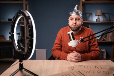 Alüminyum folyo şapkalı aptal paranoyak erkek vlogger sosyal medya kayıtlarında blog için komplo teorileri paylaşıyor. Boşluğu kopyala