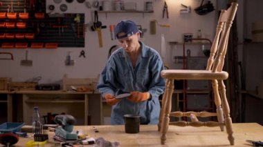 Mobilya yenileme, diy ve hobi konsepti. Atölyedeki mobilyaları yükseltmek. Orta yaşlı kadın tahta sandalye boyuyor.