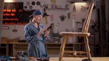 Mobilya yenileme, diy ve hobi konsepti. Atölyedeki mobilyaları yükseltmek. Cep telefonu kullanan bir zanaatkar kadın