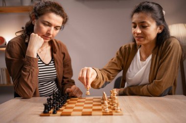 Rahatlık, strateji ve dostluk kavramı. Evde satranç oynayan, kaliteli zaman geçiren, birbiriyle bağ kuran ve birbirine meydan okuyan iki kadın.