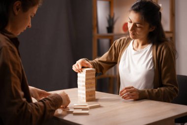 Female friends playing wooden blocks table game at home having fun leisure spending time together.Copyspace