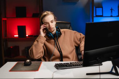 Streamer bir telefon görüşmesi yapmak için oyun oturumunu durdurur, kulaklıkları boynuna takarak birden fazla iş yapar, gece yarısı video oyunu yayınına ara verdiğinde odaklanmış iletişimi yansıtır. Boşluğu kopyala