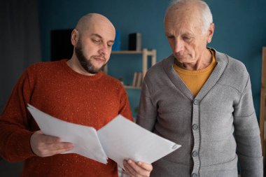 Emekli baba, yetişkin oğluyla oturma odasında mali belgeleri tartışıyor. Yaşlılara yardım etme kavramı