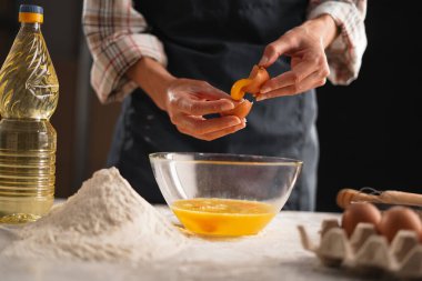 Un ve mutfak aletleriyle çevrili bir kaseye yumurta kıran eller ev yapımı pişirme, aşçılık yaratıcılığı ve mutfak blogu kavramının özünü yakalıyor..