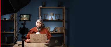 Koruyucu folyo şapkalı garip bir adam komplo teorisi mesajıyla pankart tutuyor. Ticari video bloğu, vlog kaydedici iş kursu. Komplo teorisi ve sahte haber konsepti. Pankart