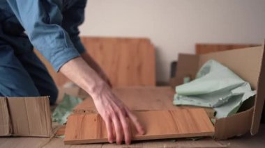 Mobilyaları kendi elleriyle monte ediyor. Karton kutuları açan bir adam oturma odasının zemininde detayları tutuyor. Yakın plan.