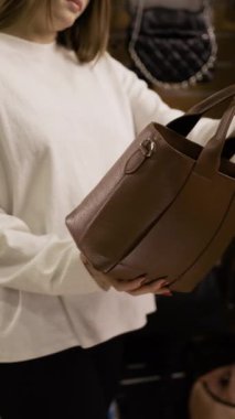 Moda aksesuarları ve alışveriş konsepti. Dükkanda deri çanta seçen genç bir kadın. Dikey video