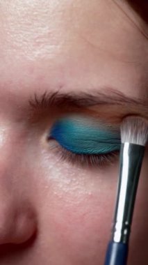 Makyajcı kadın gözkapağına mavi göz farı sürüyor, yakın plan.