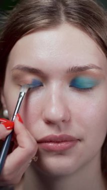 Makyaj sanatçısı, genç bir kadına makyaj yaparken güzellik salonunun göz kapağını boyuyor. Boşluğu kopyala