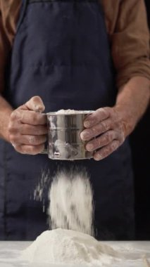 Geleneksel pişirme sürecine odaklanmak için unları ahşap bir masaya elemek için el ele tutuşun. Sahnede özgün yöntemler, eski moda tarifler ve zanaatkarlık vurgulanıyor.