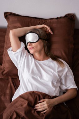 Yatakta uzanmış, göz maskesi takan yaşlı bir kadın. Boşluğu kopyala