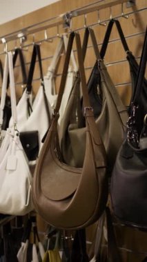 Moda butiğinde metal raflarda asılı moda deri çantaları koleksiyonu, değişik şekiller, boyutlar ve nötr renkler, modern tarz için zarif aksesuarlar.