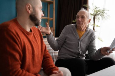 Aile, duygular ve iletişim konsepti - yaşlı baba evdeki belgeler hakkında oğluyla duygusal olarak tartışıyor, emeklilik evrakları sırasında hayal kırıklığını ve şaşkınlığı dile getiriyor
