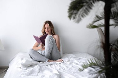 Güzel sarışın kadın günlük notları okuyor beyaz yatağında rahat bir yatakta oturuyor. Boşluğu kopyala